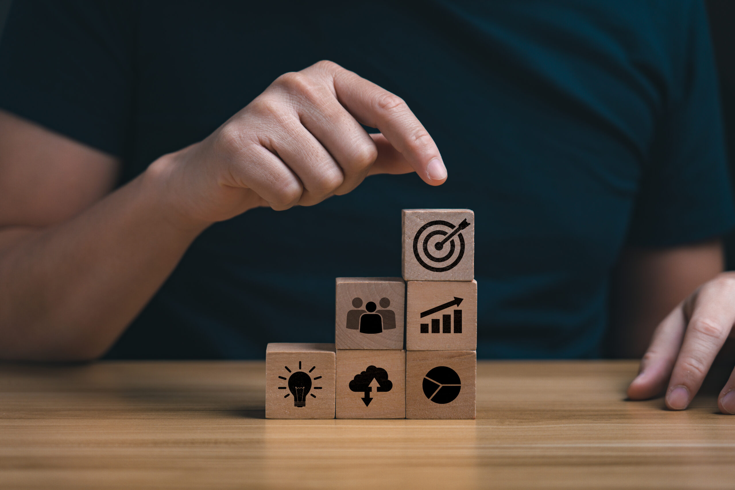 Businessman's hand selects a target icons on wooden cubes, business development concept. business strategy and action plan, goals for success, management